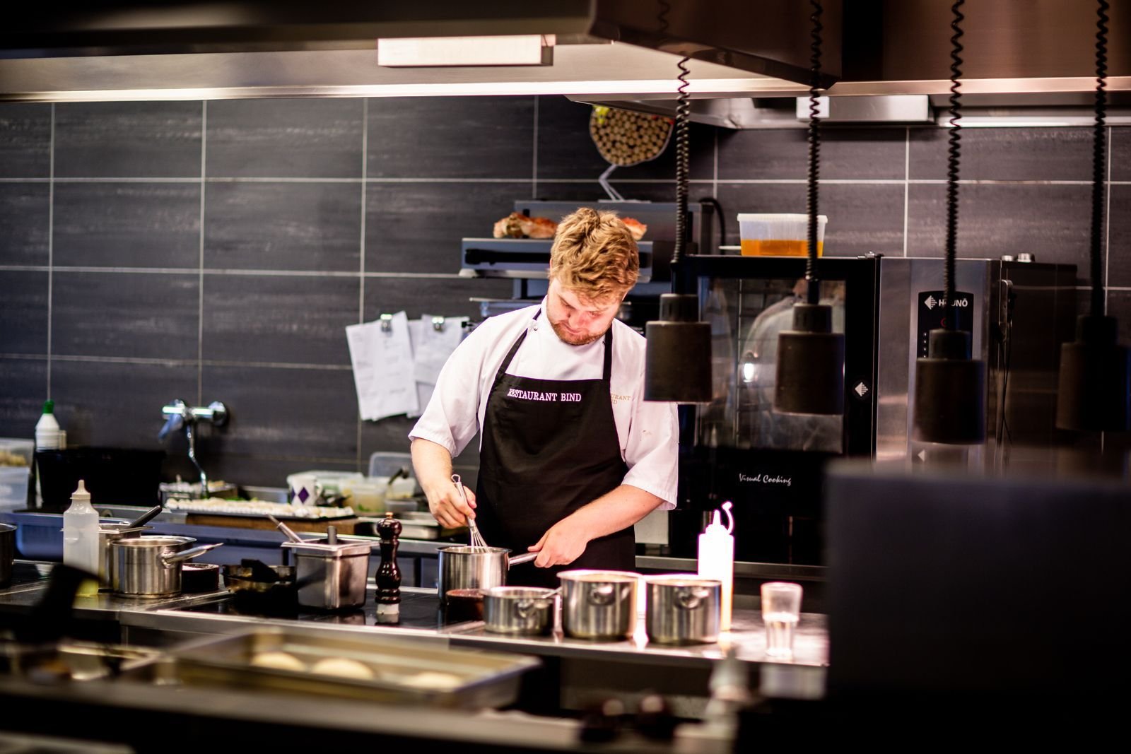 Cooks working a busy commercial kitchen line beneath a stainless steel exhaust hood.