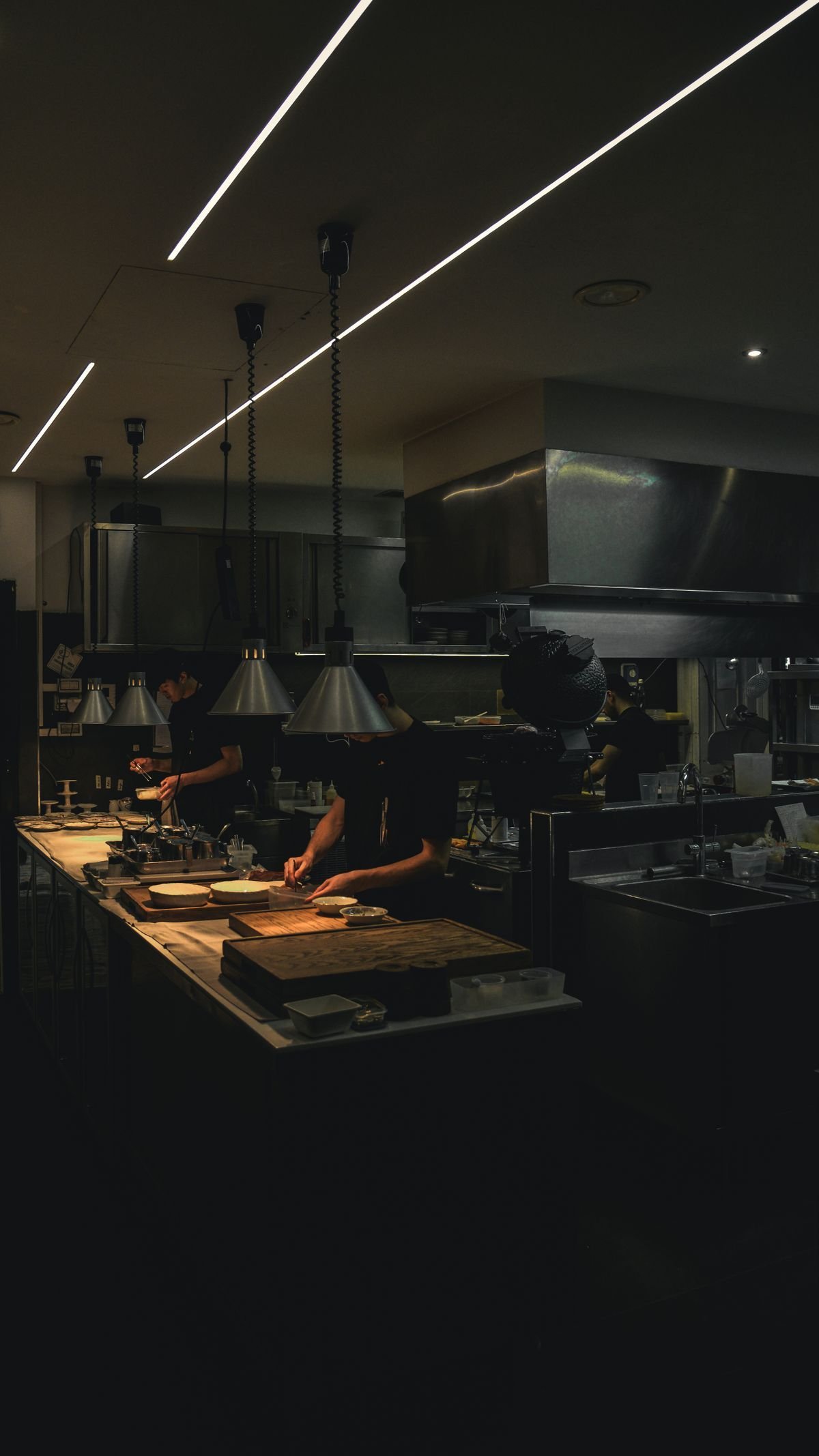 Cooks working beneath a stainless steel exhaust hood on a commercial kitchen line.